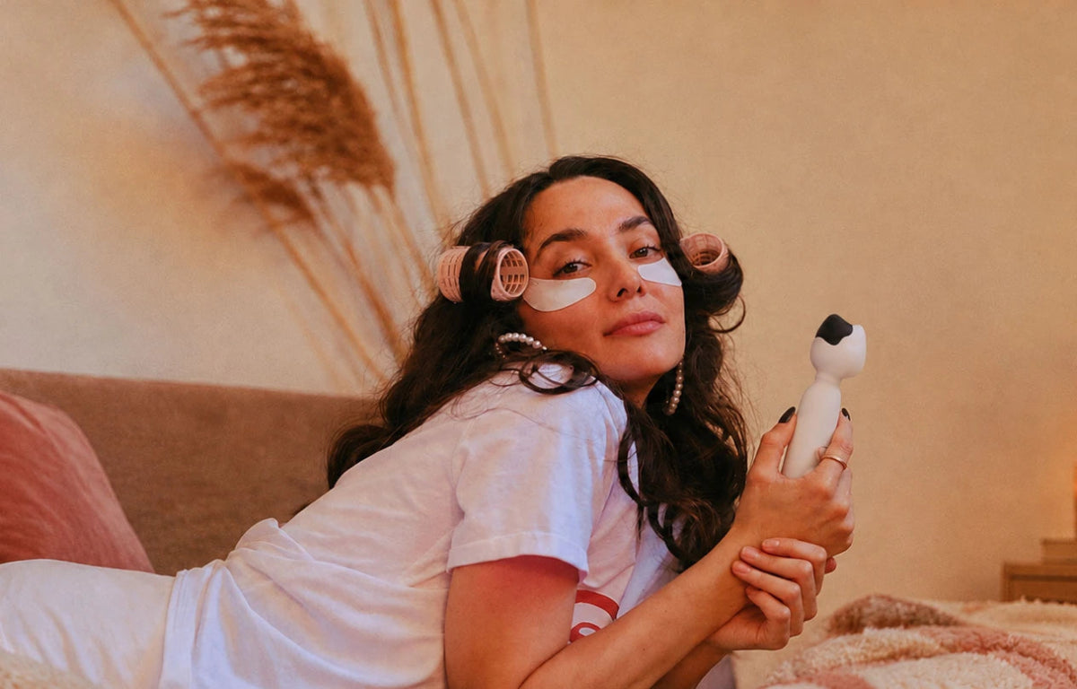 Woman holding the Mesanel cat-head wand vibrator in a cozy bedroom setting